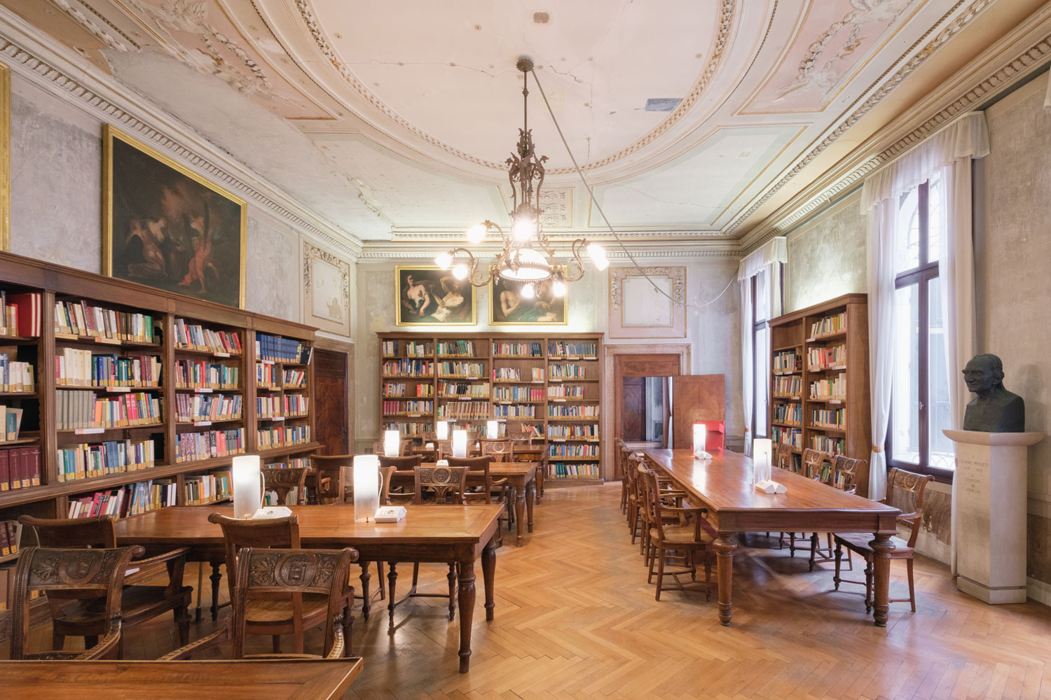 Sala di lettura della Biblioteca della Fondazione Querini Stampalia a Venezia con scaffali di libri, tavoli in legno e lampadario storico